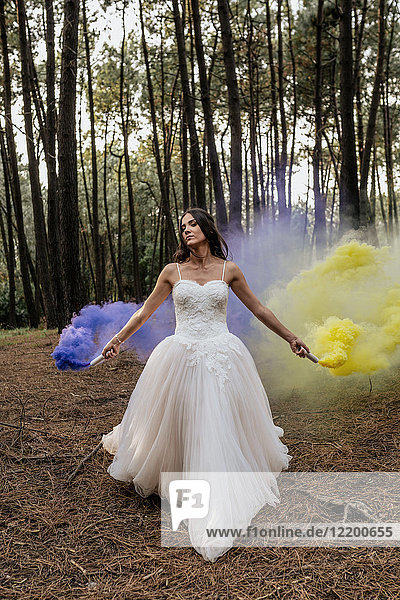 Woman wearing wedding dress in forest holding smoke torches