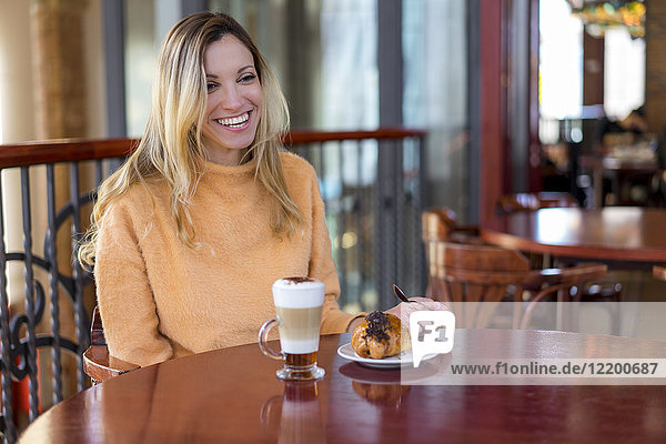 Fröhliche junge Frau in einem Café bei Kaffee und Gebäck