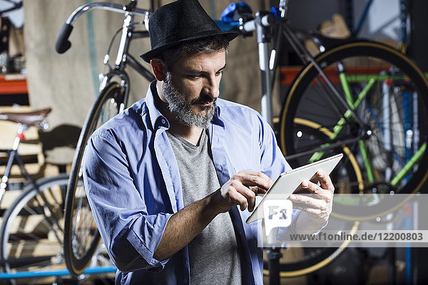 Mann in der Fahrradwerkstatt mit Tablette