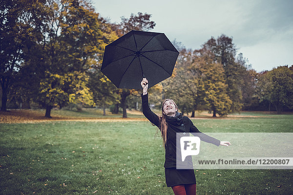 Junge Frau tanzt mit Regenschirm im herbstlichen Park