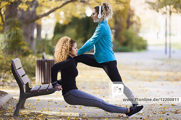 Two sportive young women stretching in park