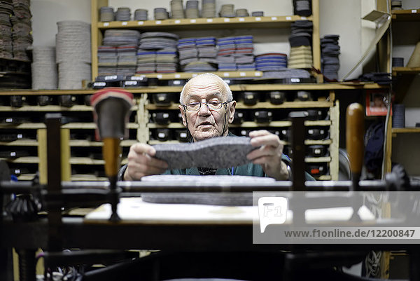 Senior-Schuhmacher mit altmodischer Stanzmaschine in der Werkstatt