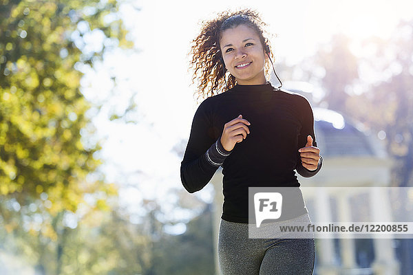 Smiling young woman with earphones running in park