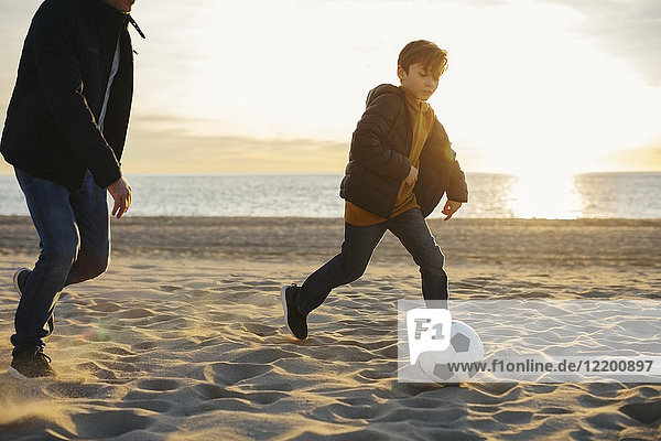 Father and son playing football on the beach at sunset