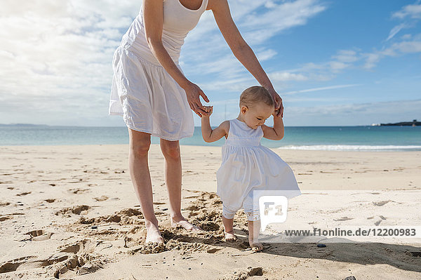 Mutter hilft der kleinen Tochter  die am Strand spazieren geht.