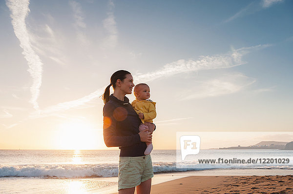 Mother holding little daughter on the beach at sunset