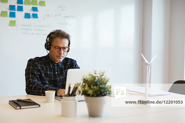 Geschäftsmann mit Kopfhörer über Laptop am Schreibtisch im Büro