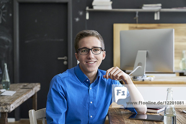 Porträt eines lächelnden jungen Mannes am Holztisch im Büro
