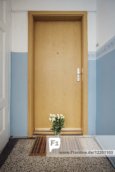 Vase with bunch of white farewell flowers on floor mat at apartment door of deceased neighbour