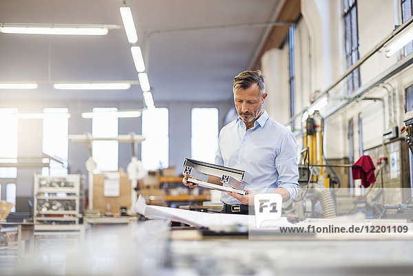 Mature businessman in factory examining component