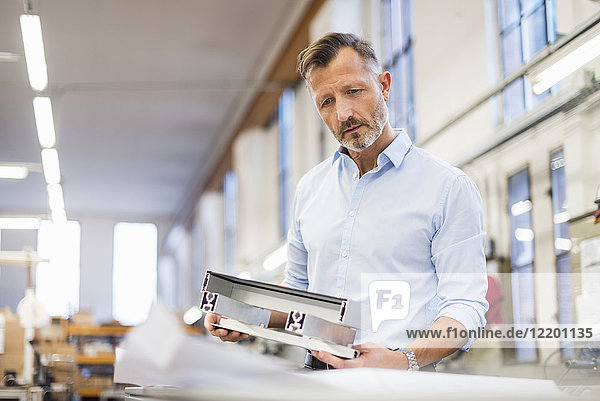 Mature businessman in factory examining component