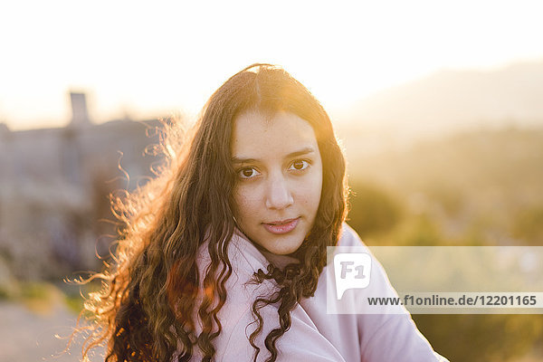 Portrait of young woman with long curly hair at sunset