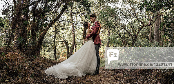 Braut und Bräutigam stehen im Wald und umarmen sich.