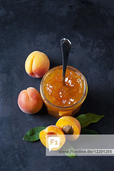 Glas Aprikosenmarmelade und Aprikosen auf dunklem Hintergrund
