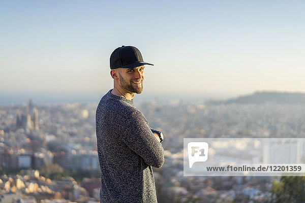 Spain  Barcelona  smiling young man standing on a hill overlooking the city