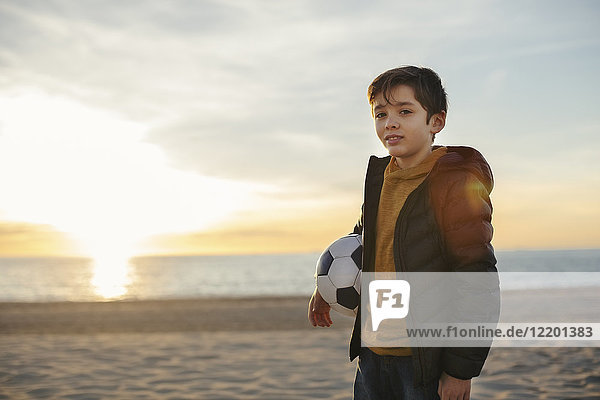 Porträt eines Jungen mit Fußball am Strand bei Sonnenuntergang