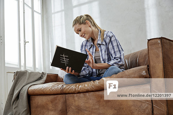 Lächelnde Frau sitzt auf der Couch mit Buch
