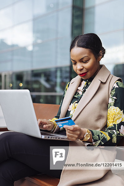 Geschäftsfrau auf der Bank sitzend mit Laptop und Kreditkarte