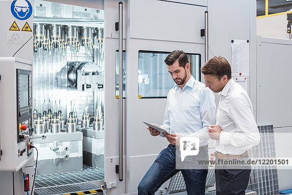 Two men standing at machine in factory looking at tablet