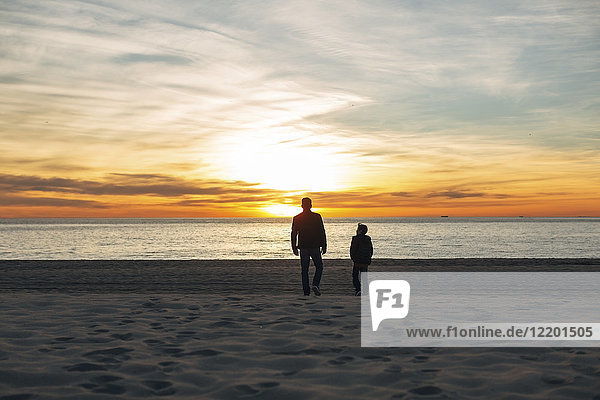 Vater und Sohn gehen bei Sonnenuntergang am Strand spazieren.