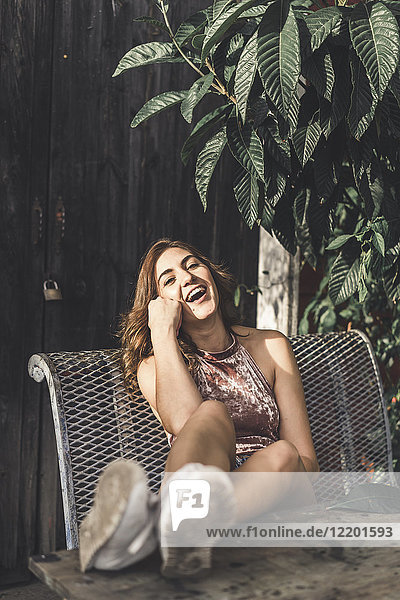 Porträt einer lachenden jungen Frau  die auf einer Bank im Freien sitzt.