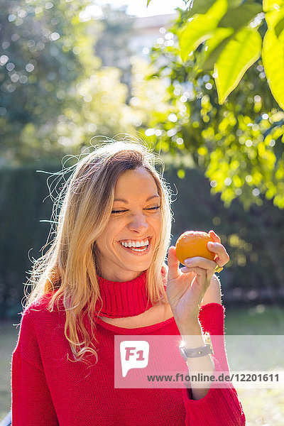 Lachende junge Frau mit Mandarine im Garten