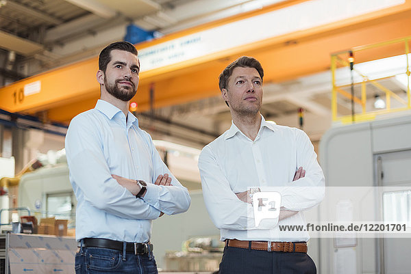 Two confident businessmen in factory looking around
