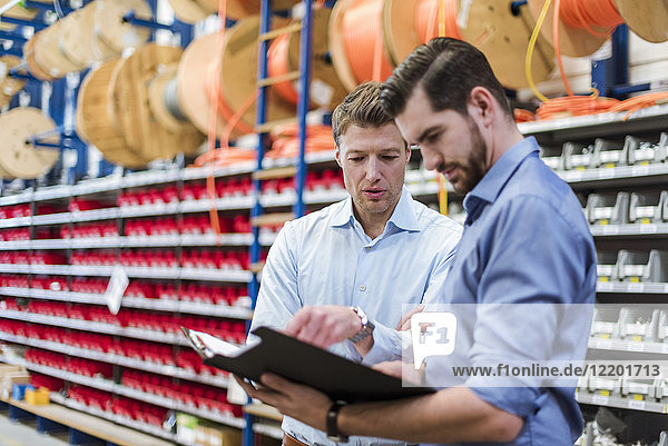 Two men with folder talking in factory storeroom