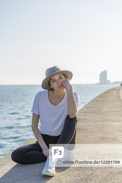 Spain  Barcelona  portrait of woman wearing hat sitting at waterfront promenade