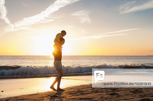 Mutter geht mit kleiner Tochter am Strand bei Sonnenuntergang spazieren