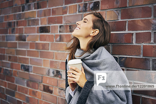 Glückliche Frau mit Kaffee vor der Backsteinmauer