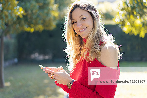Portrait of smiling young woman using smartphone in a garden