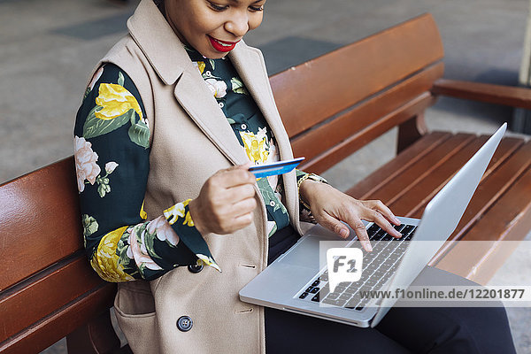 Geschäftsfrau auf der Bank sitzend mit Laptop und Kreditkarte