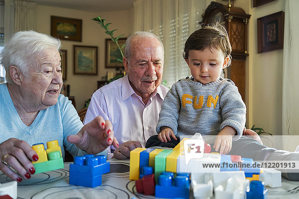 Urgroßeltern und kleines Mädchen beim Spielen mit Plastikbausteinen zu Hause