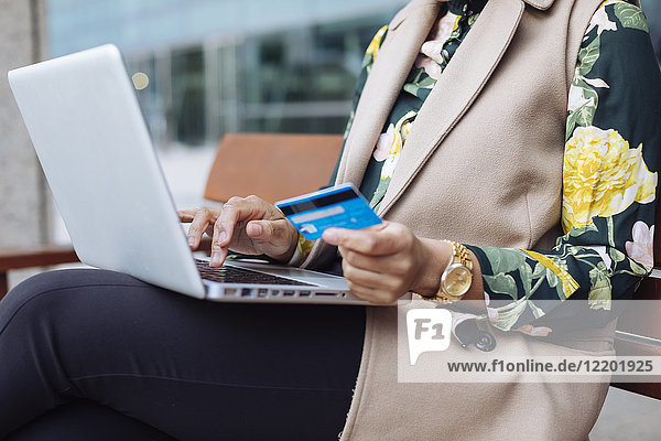 Geschäftsfrau auf Bank sitzend mit Laptop und Kreditkarte  Teilansicht