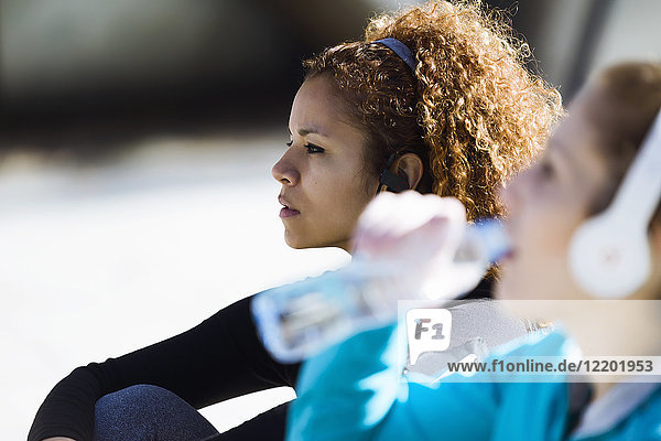 Two sportive young women having a break listening to music