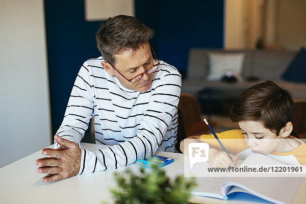 Father watching son doing homework at table