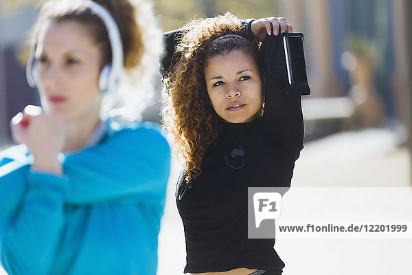 Two focused sportive young women stretching listening to music