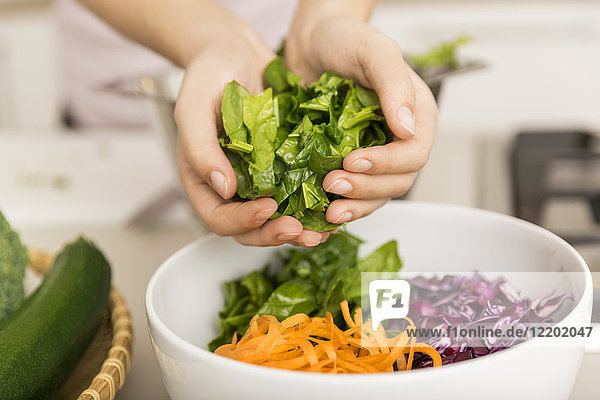 Hände legen frischen Salat in eine Schüssel mit verschiedenem Gemüse