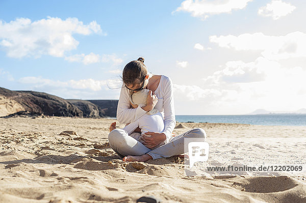 Mutter kuschelt mit kleiner Tochter am Strand