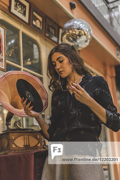 Portrait of pensive young woman standing in front of antique shop holding gramophone record