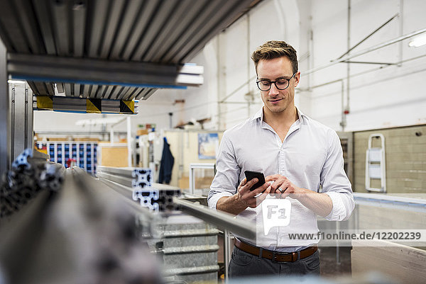 Young businessman using cell phone in factory