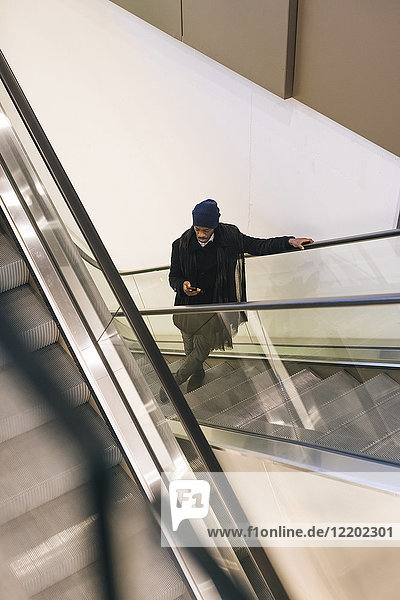 Italien  Mailand  Afroamerikaner mit Smartphone auf Rolltreppe