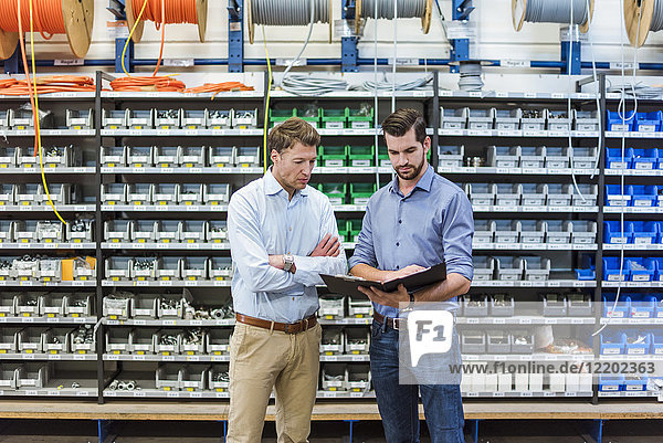 Two men with folder in factory storeroom