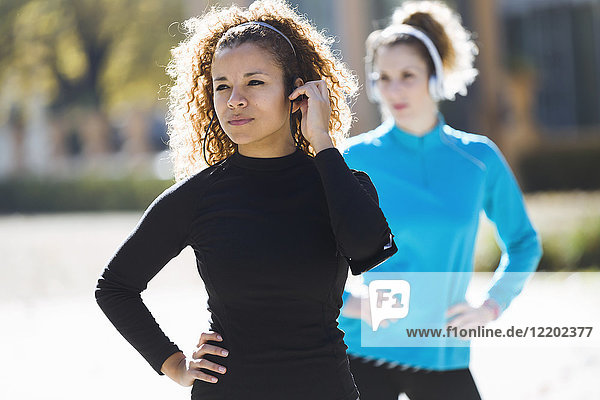 Two focused sportive young women standing listening to music