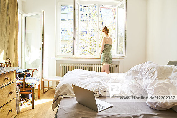 Back view of woman in bedroom looking out of window