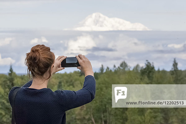 USA  Alaska  young woman photographing with smartphone Mount Denali