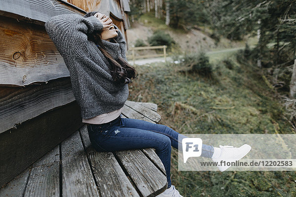 Happy young woman sitting at a wooden house in the nature