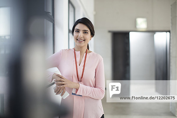 Porträt einer lächelnden jungen Frau  die auf dem Flur im Büro steht.