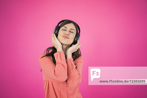 Frau vor der rosa Wand hört Musik über Kopfhörer